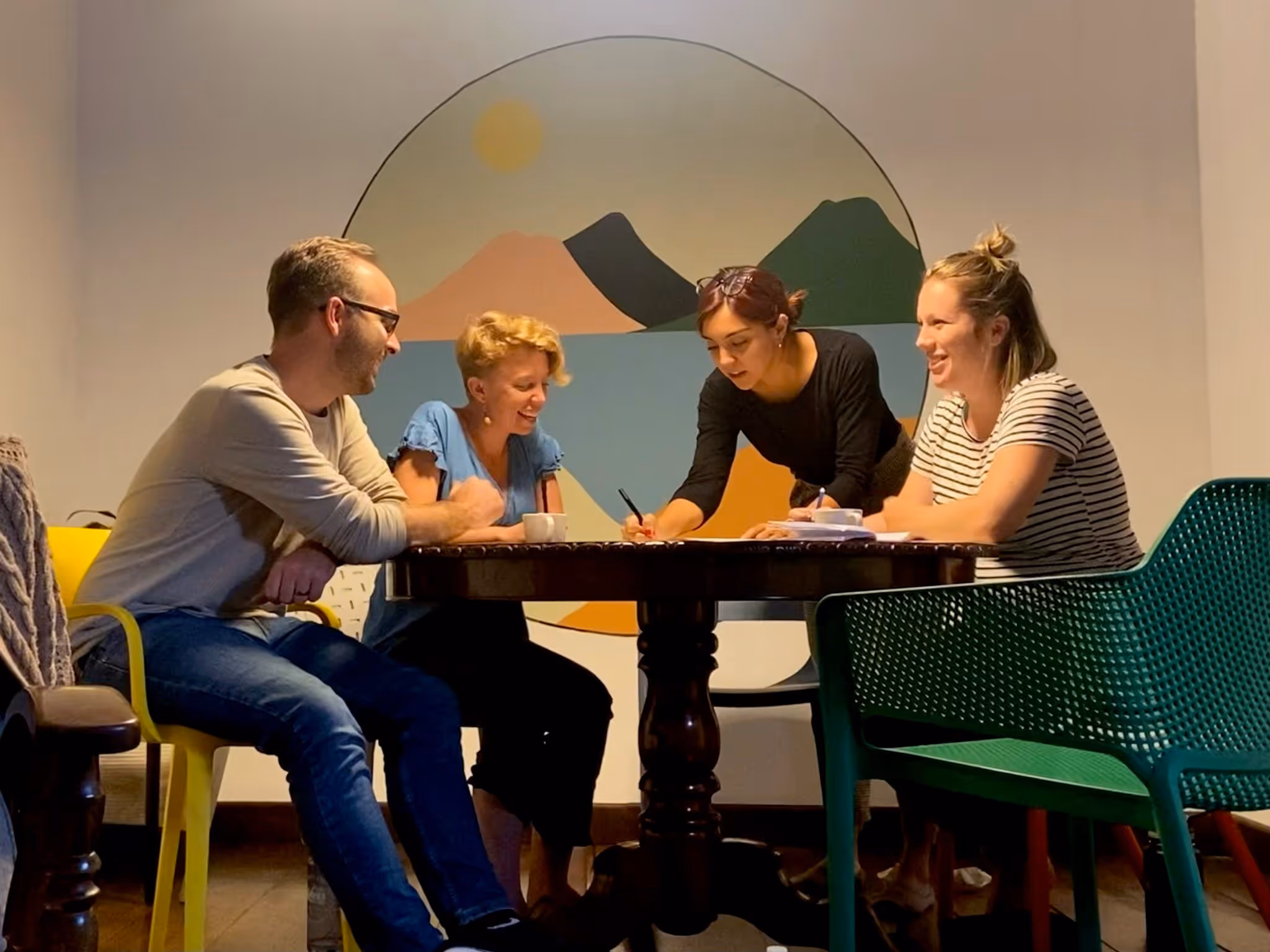 Four people around a table working together, with wall art of mountains and sun behind them.