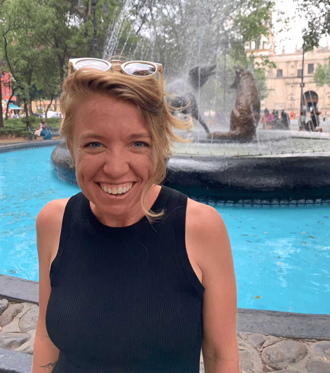 Rebecca Nash with short blond hair and sunglasses on head near a fountain with bear statues.