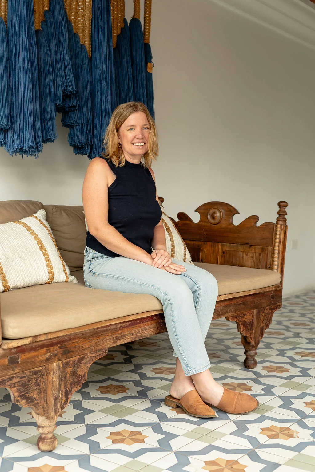 Rebecca Nash, founder of Mae North, smiling on a wooden daybed.