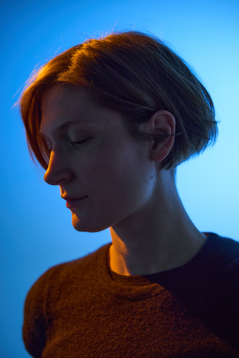 Portrait of Lisa Schatz with short hair and closed eyes illuminated by blue and orange lighting.