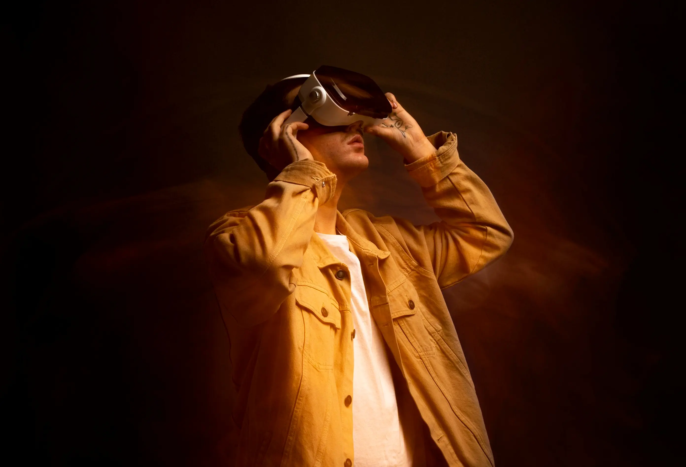 Man wearing a tan jacket and white shirt using virtual reality headset on dark background.