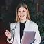 Smiling female healthcare professional in a white lab coat and stethoscope holding a clipboard.