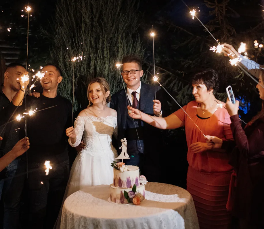 Bride and groom with guests holding sparklers around a wedding cake at nighttime outdoor celebration.