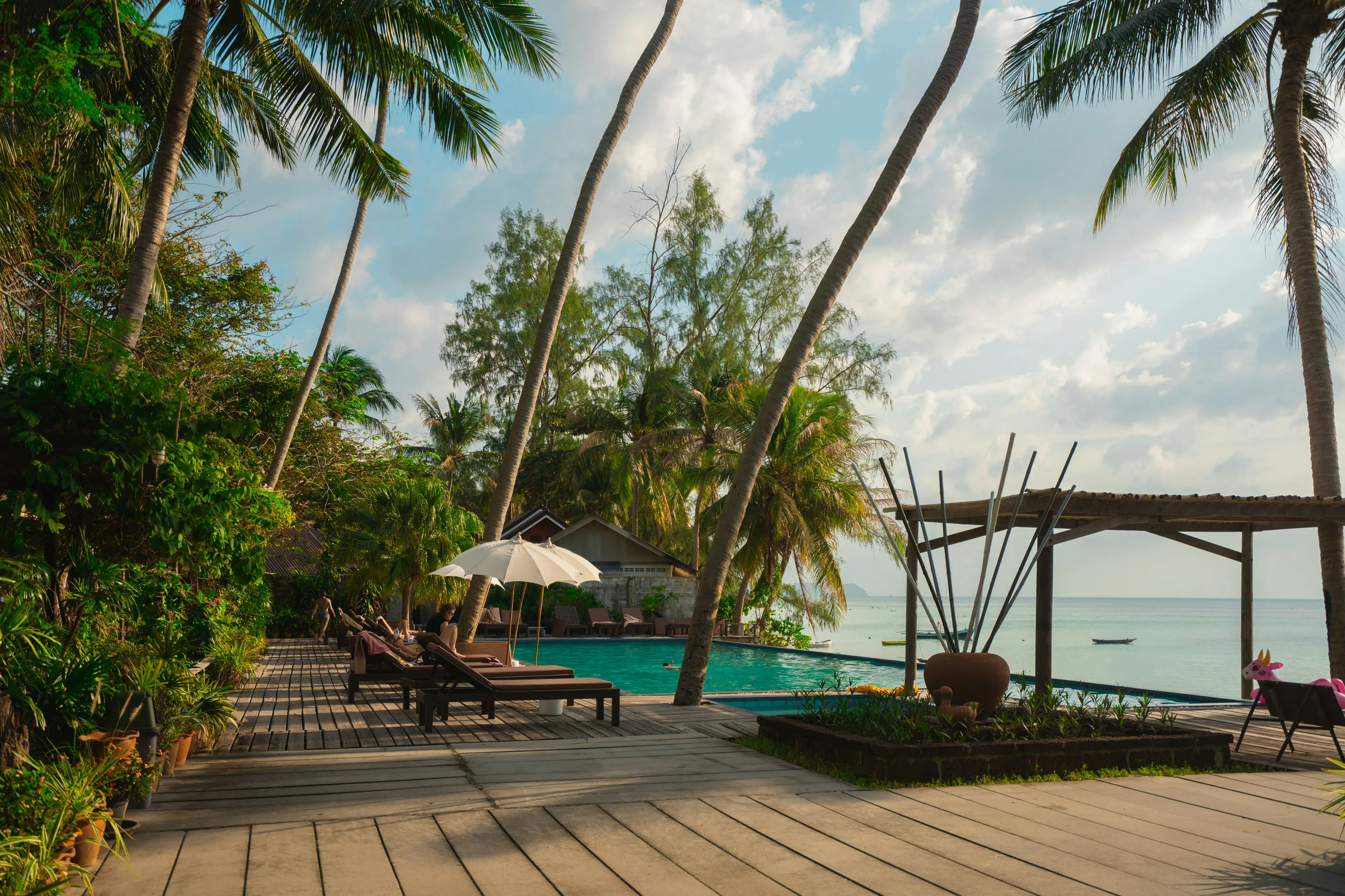 Relaxing tropical resort pool area with palm trees, lounge chairs, umbrellas, and ocean view.