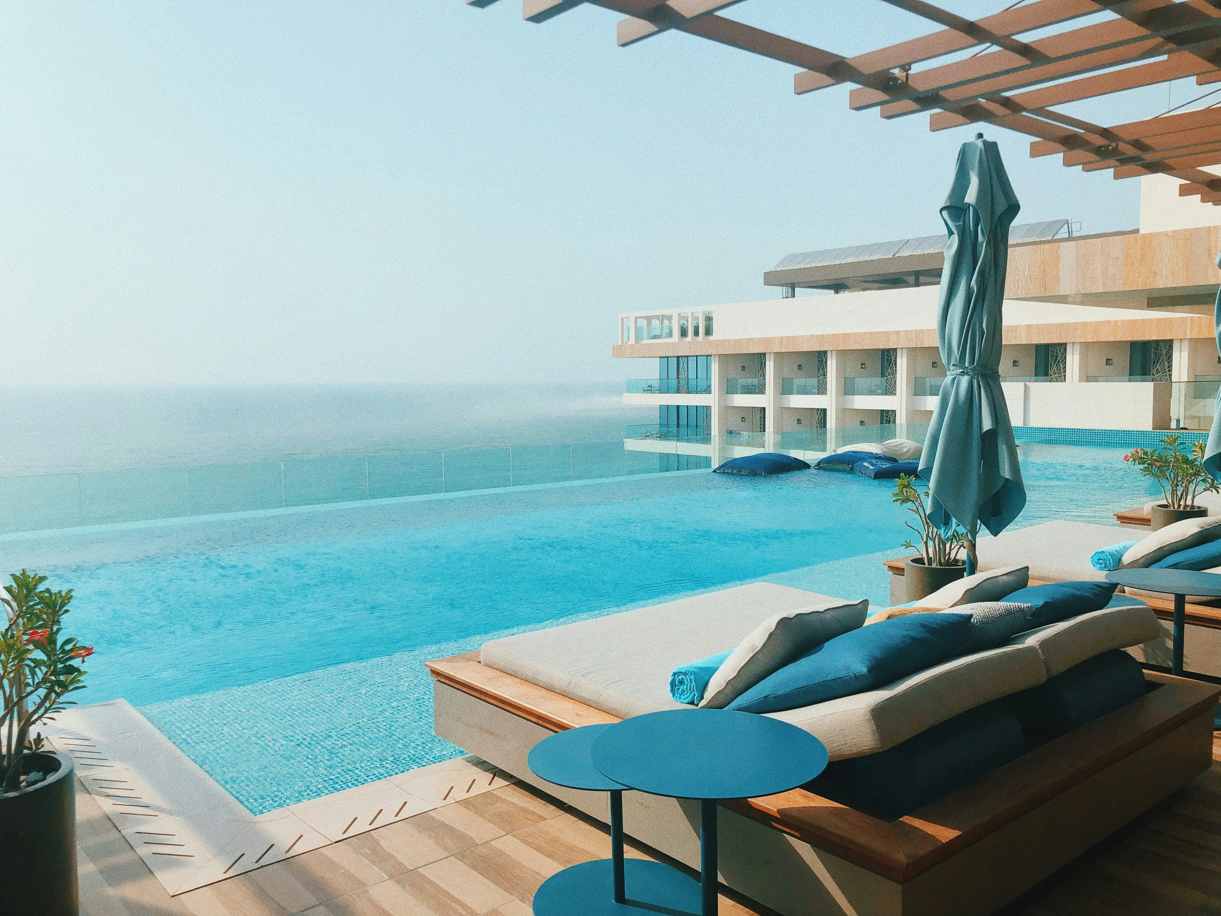 Infinity pool with blue water overlooking the ocean, surrounded by lounge chairs with blue cushions and closed umbrellas.