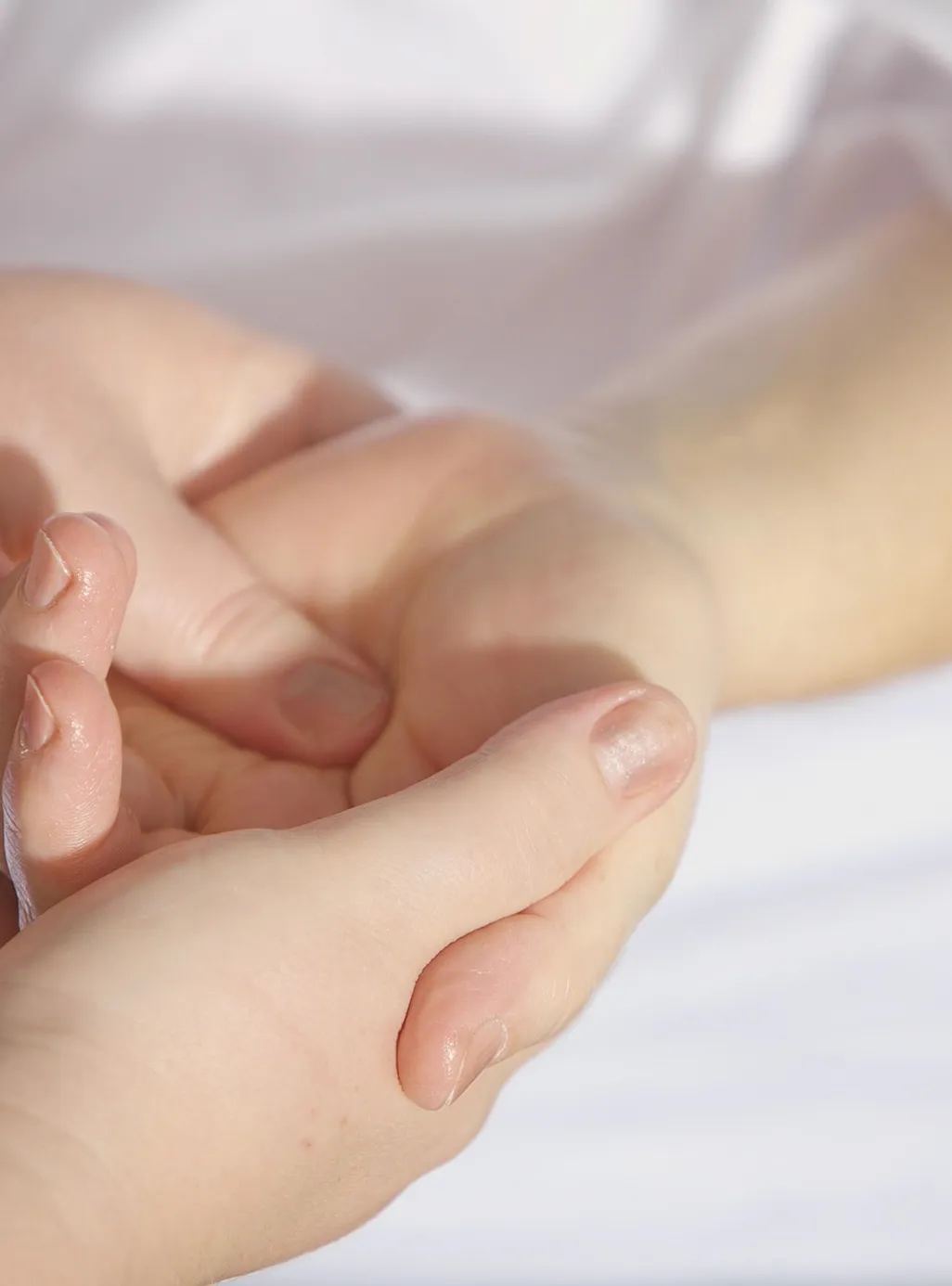 Close-up of two hands gently holding each other on a light background.