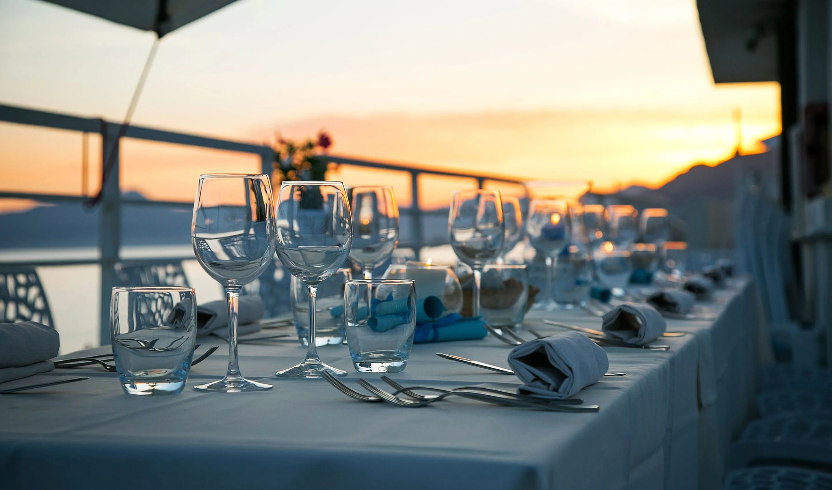 Outdoor dining table set with glassware, silverware, and napkins during sunset.