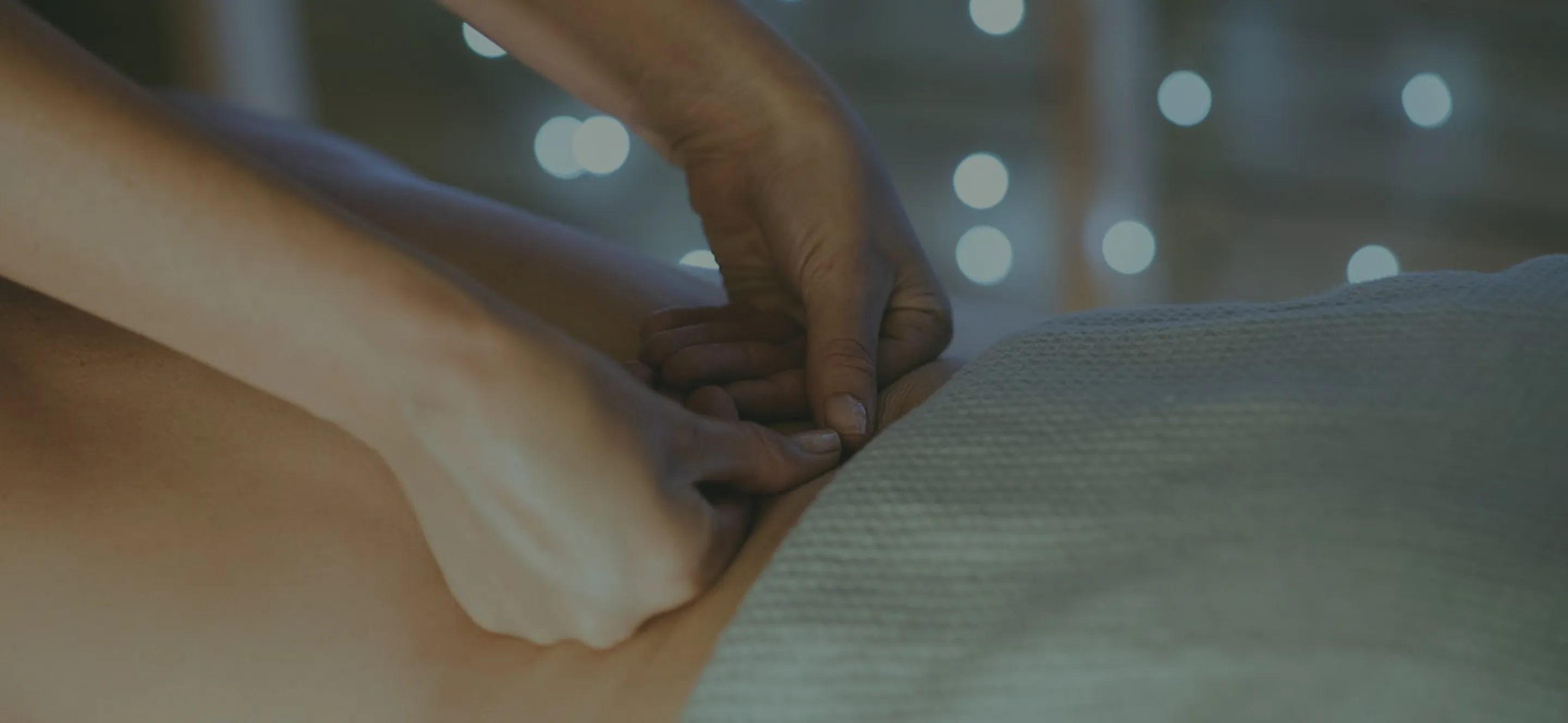 Hands giving a back massage with soft lights in the background.