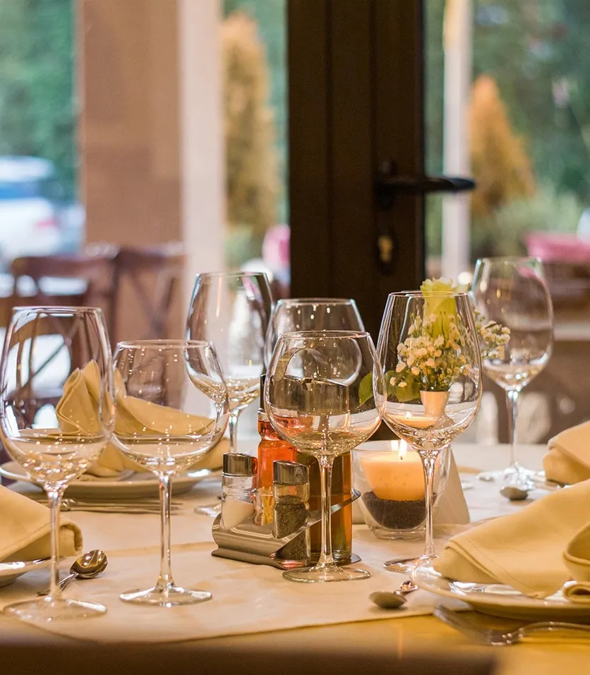 Dining table set with multiple empty wine glasses, folded napkins, cutlery, a candle, and small flower arrangement in a cozy restaurant.