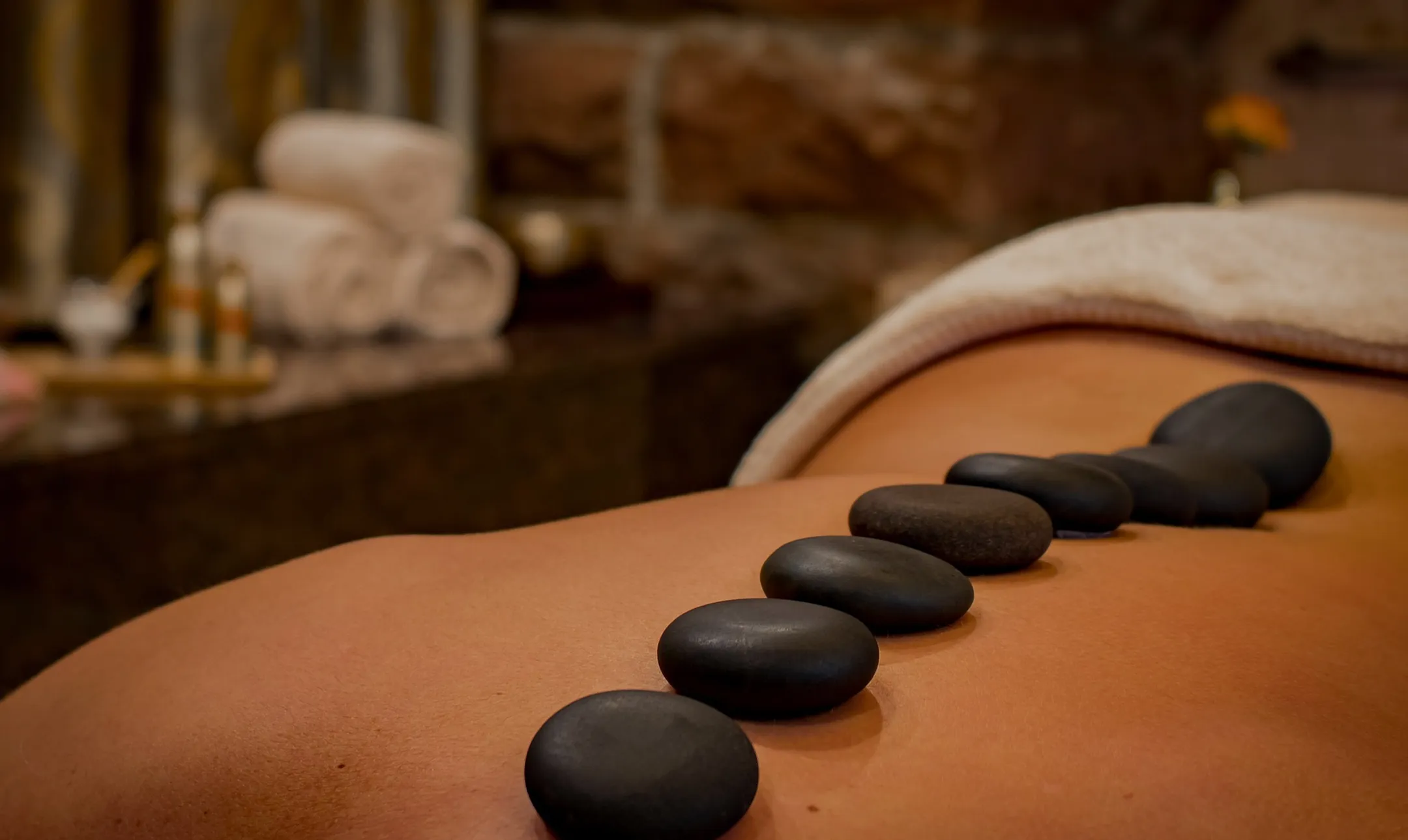 Row of smooth black massage stones arranged on a person's back in a spa setting.