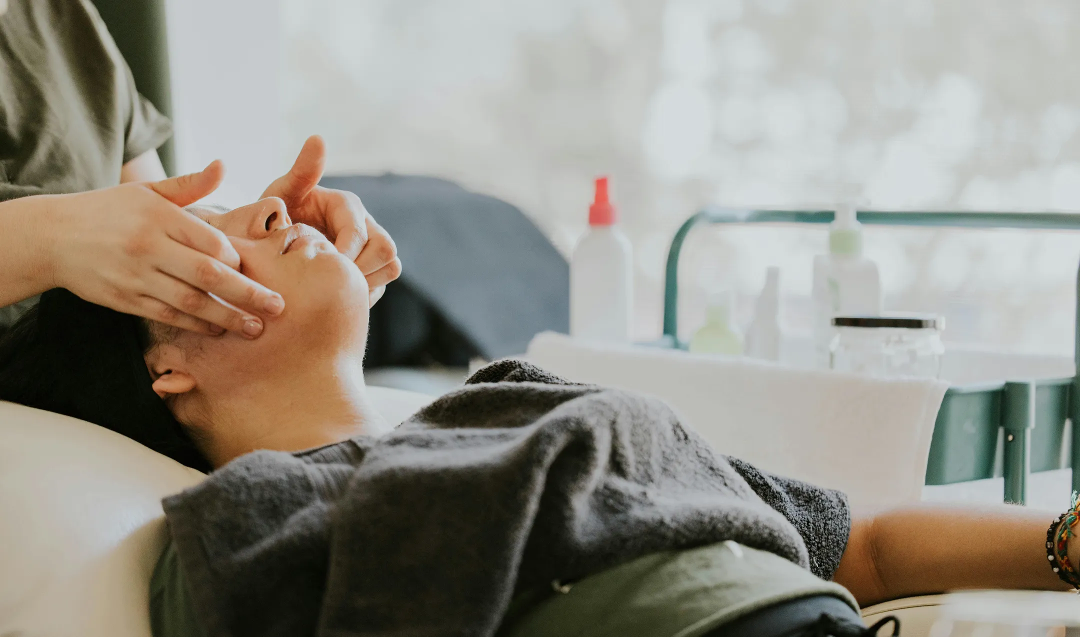 Person receiving a facial massage while lying down with a towel over their chest.
