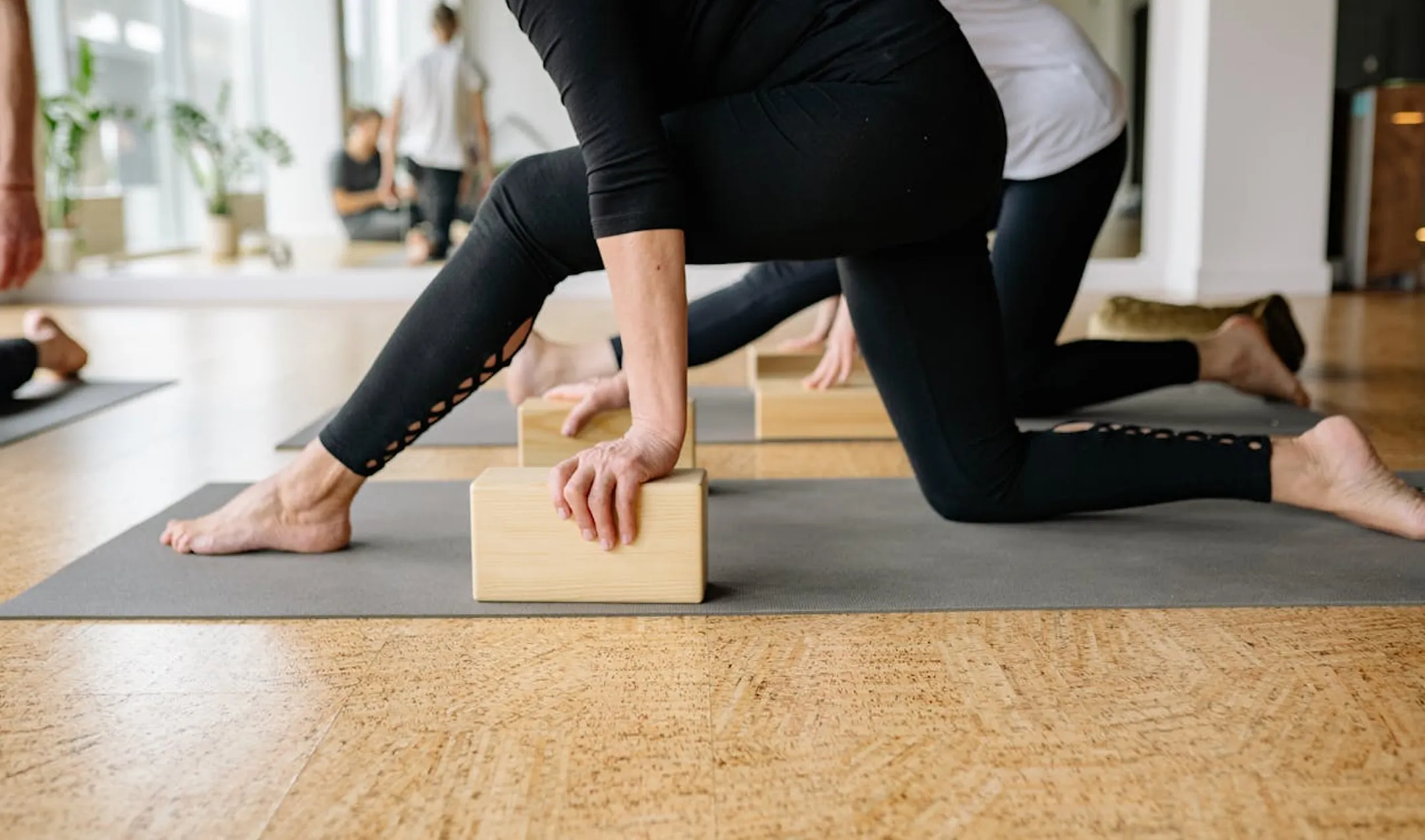 People practicing yoga in a studio using wooden blocks for support during a stretching pose on mats.