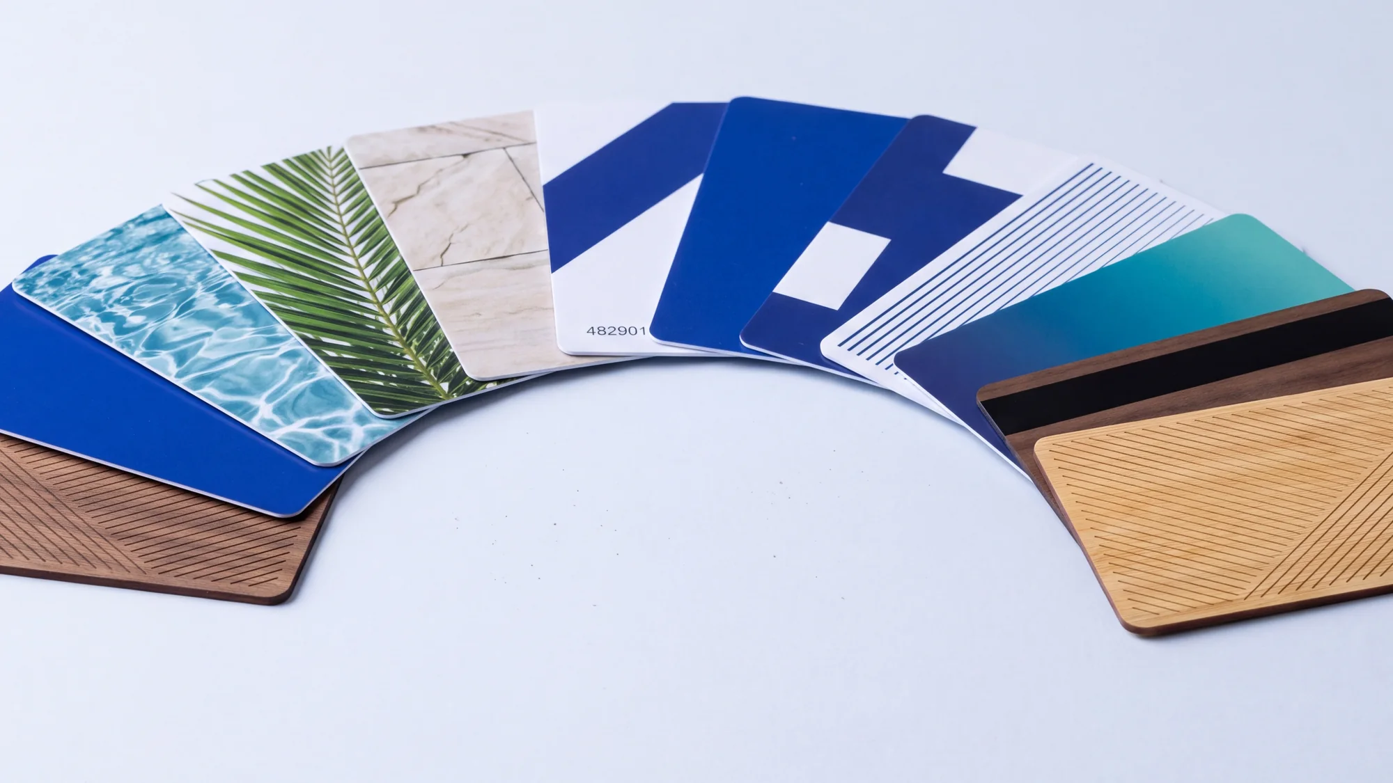 Fourteen RFID cards fanned out across a table in a production run, printed in different designs, with laser engraved walnut and bamboo cards among them.