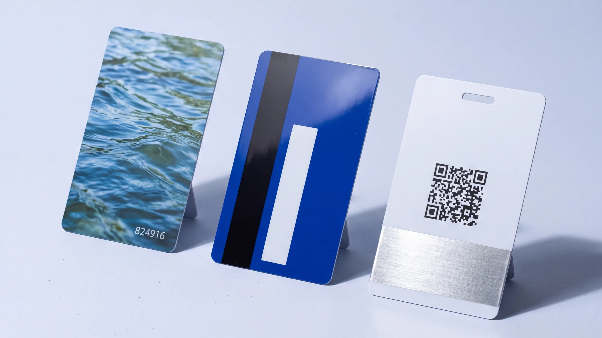 Three cards standing in a row: a matte card with a full colour photographic print and a serial number, a gloss card with a magnetic stripe and signature panel, and a card with a QR code, a silver foil band and a punched lanyard slot.