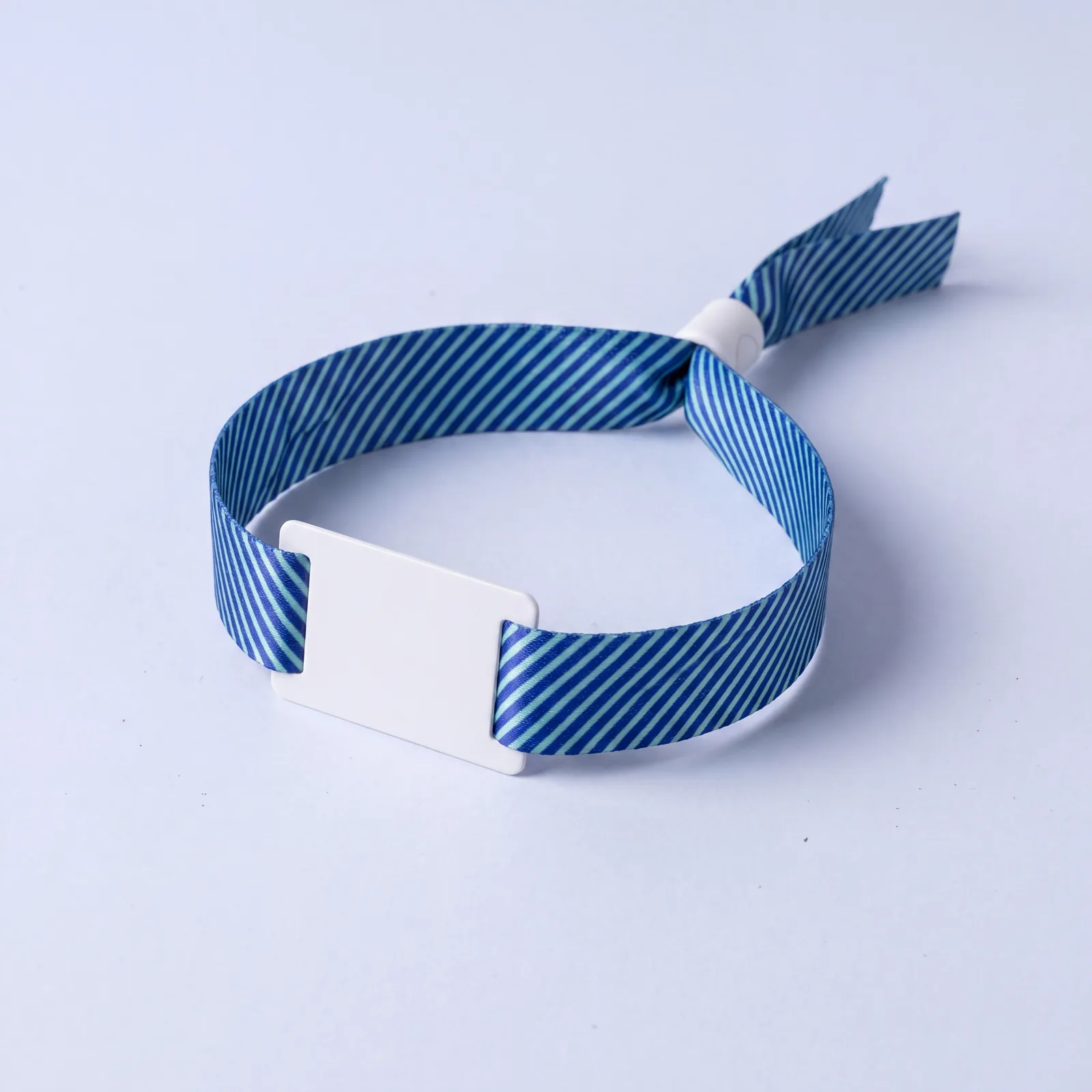A blue fabric event wristband with a white plastic tag and a one-way bead closure