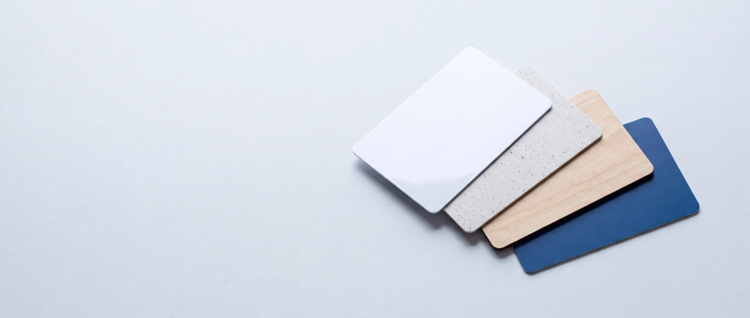 Four blank cards fanned out in gloss PVC, recycled PVC, wood and matte blue