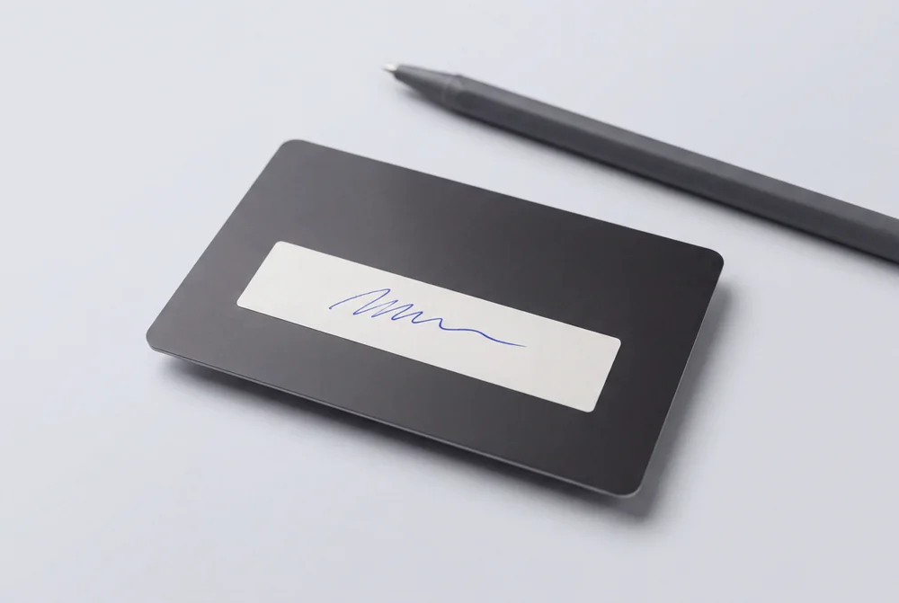 Dark card with a white signature panel signed in blue ballpoint, with a pen alongside