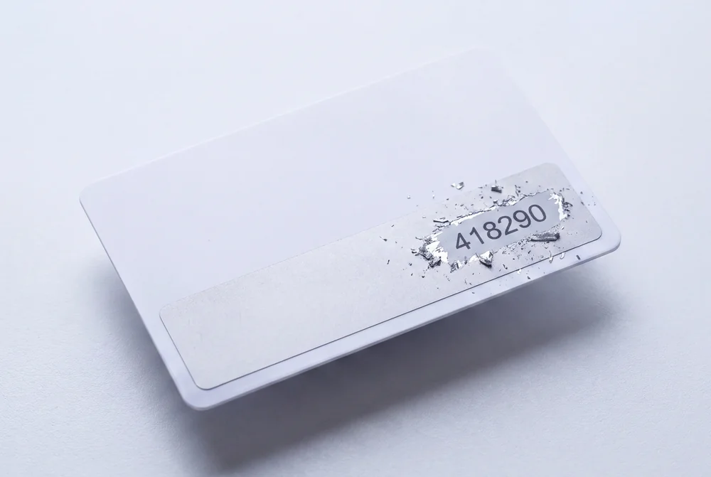 Scratch panel on a white card partly scratched away, revealing the code printed underneath