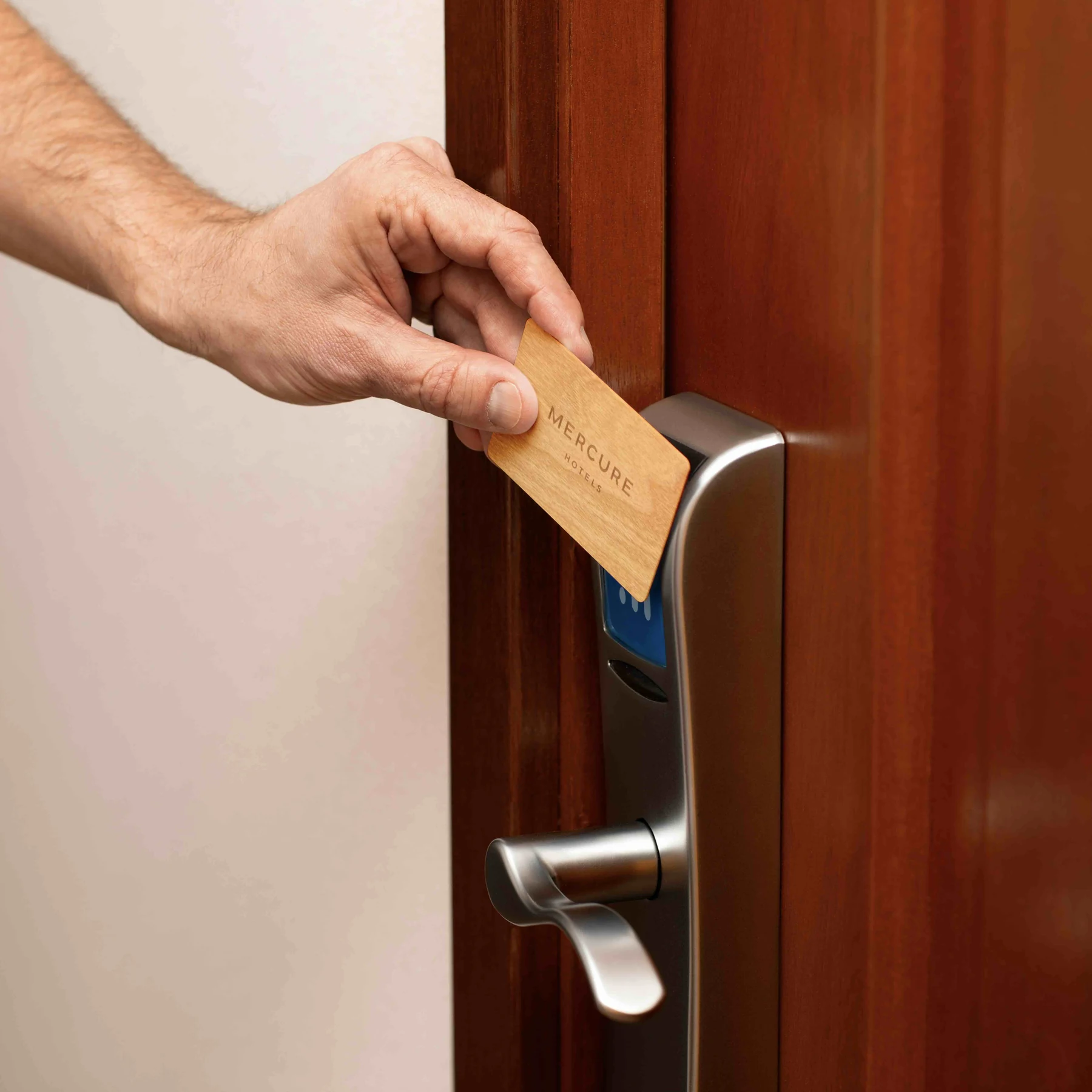 A guest holds a wooden RFID key card to a guest room lock