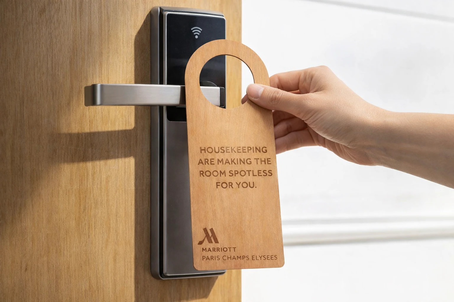 A wooden door hanger being hung on a guest room door handle