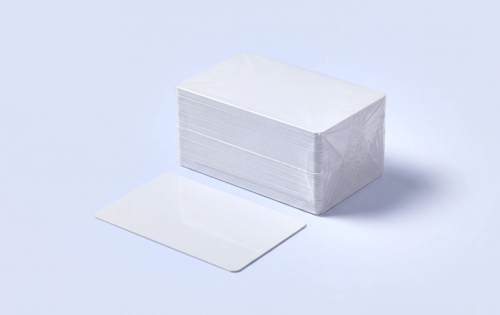 A shrink wrapped brick of blank white PVC cards with a single loose card in front of it