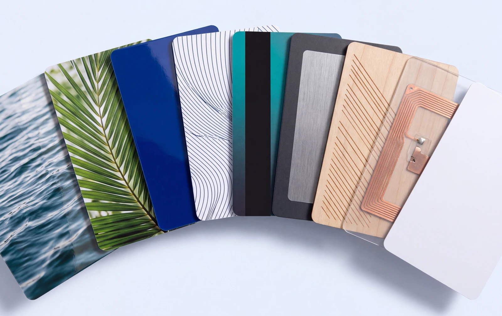 Nine blank RFID and NFC cards fanned out, showing gloss, matte, metallic, wood and a clear inlay with the antenna visible