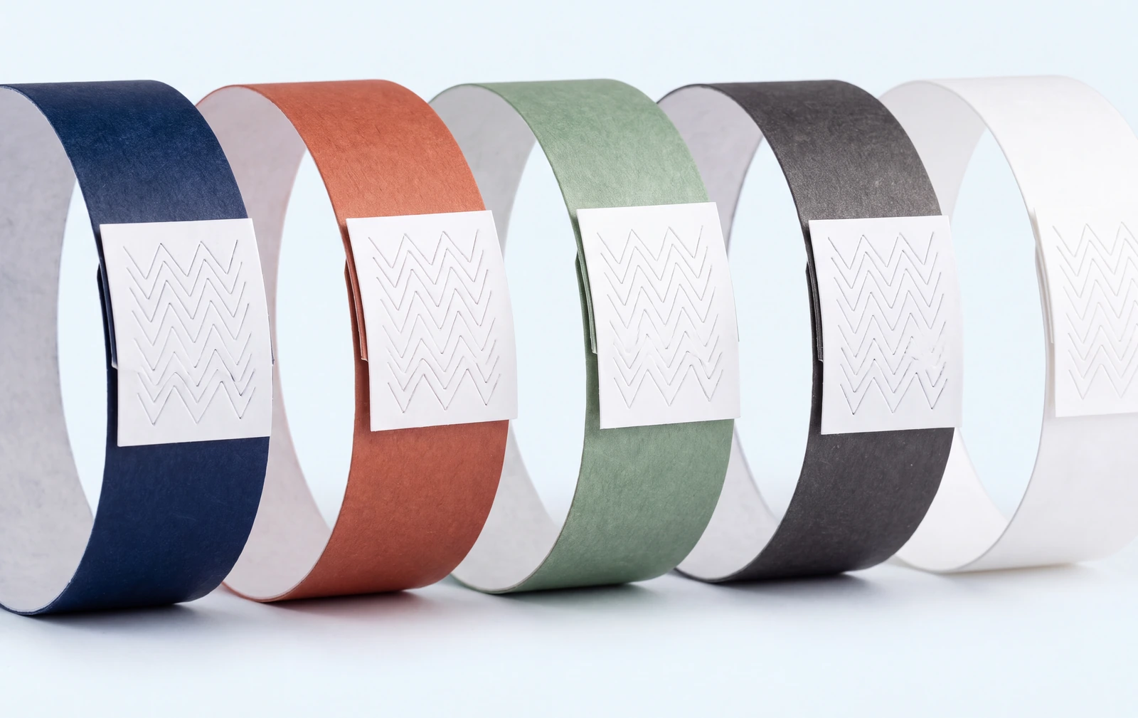 Tyvek event wristbands closed into rings in navy, terracotta, sage, charcoal and white, each with its white tamper evident tab
