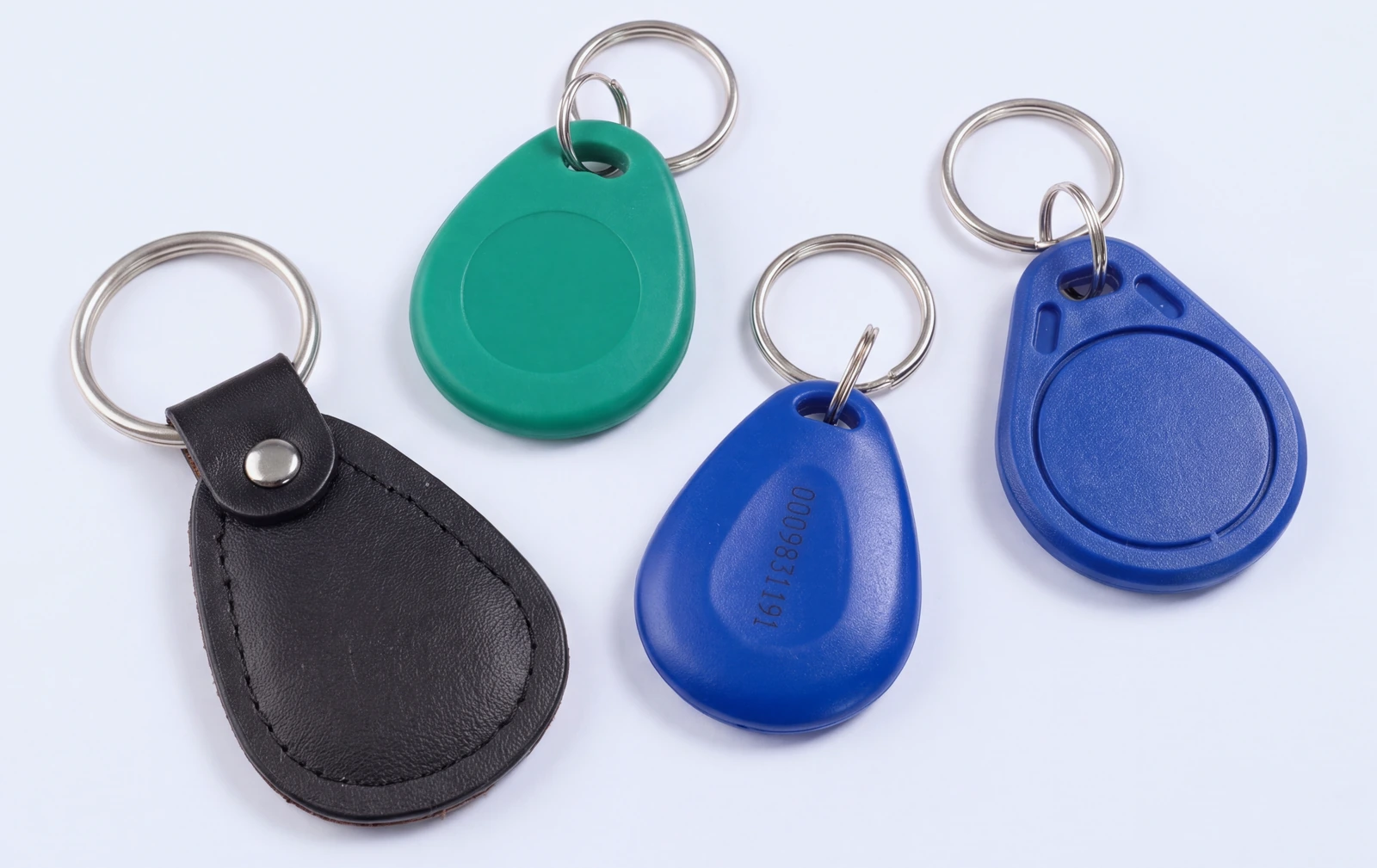 Four RFID key fobs, three in moulded ABS in blue and green and one in black leather, each on a steel split ring