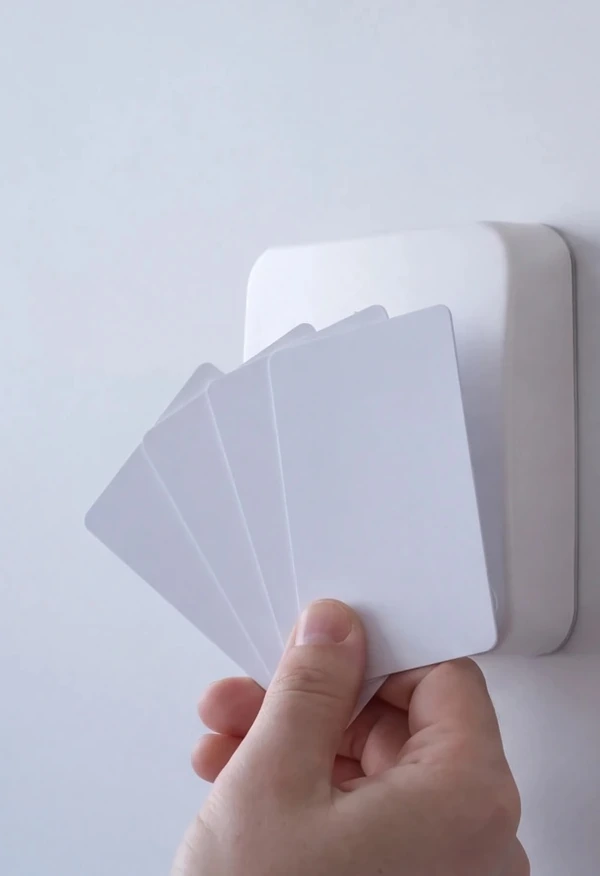 A hand holding four blank white cards up to a wall-mounted access control reader