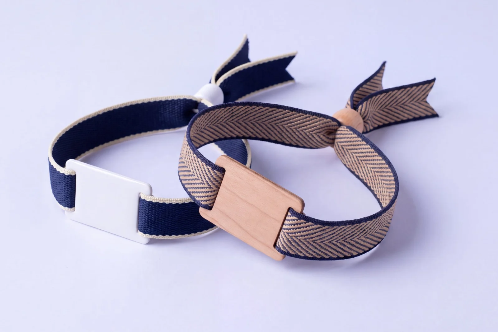 Two woven RFID wristbands: navy fabric with a white PVC tag, and herringbone fabric with a wooden tag and wooden bead closure