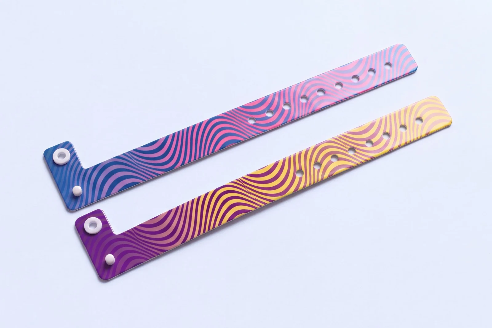 Two vinyl resort wristbands with a printed wavy line pattern, one in blue and pink and one in purple and yellow, each with a white snap stud and adjustment holes