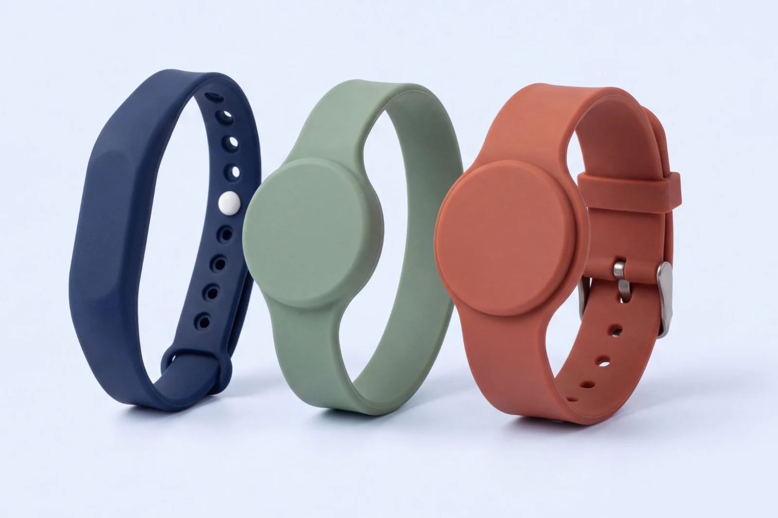 Three RFID silicone wristbands: a navy adjustable strap with a snap stud, a sage green one-piece band with a round head, and a terracotta watch-style band with a round head and metal buckle