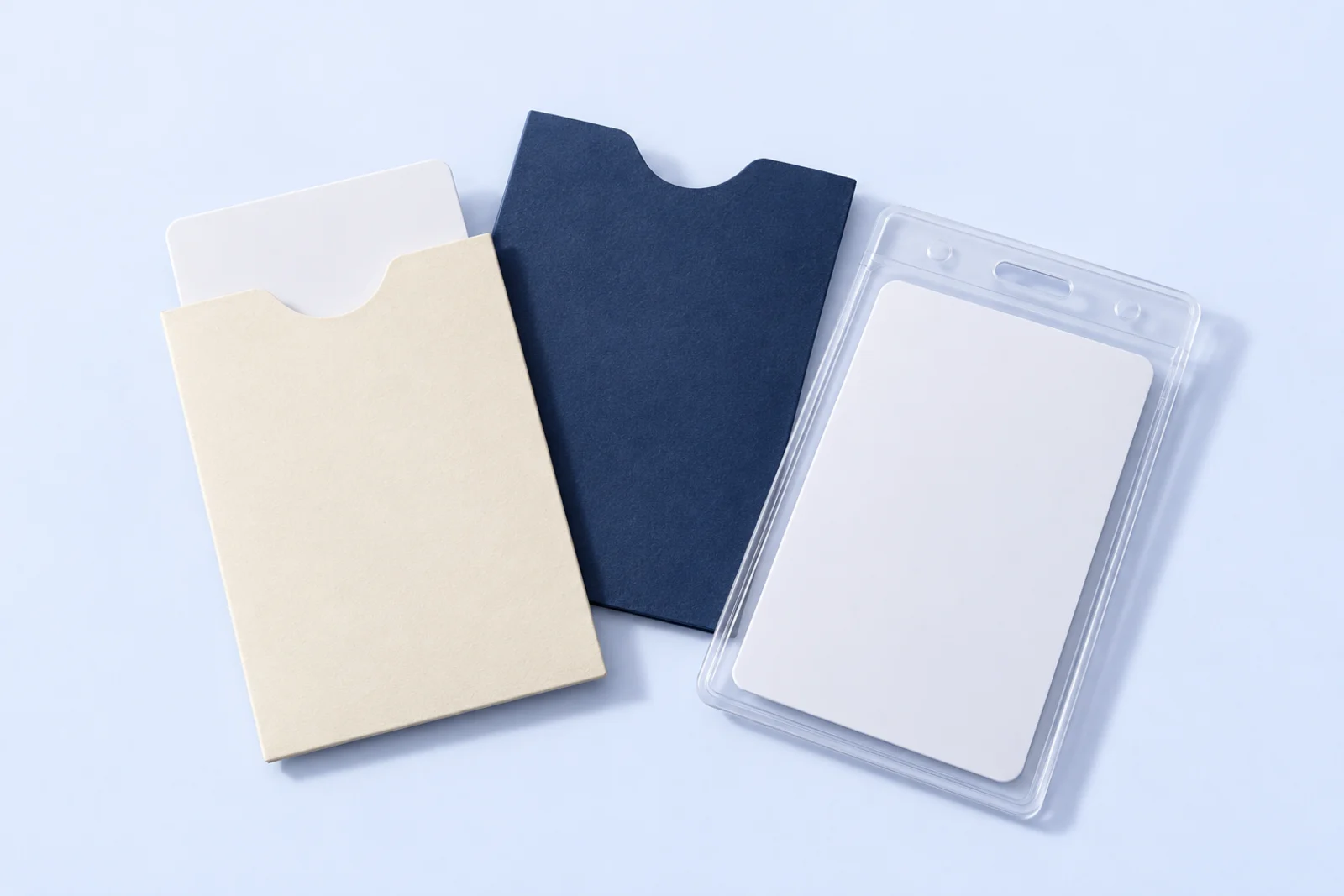 Card holders: a cream paper key card sleeve with a card inside, a navy paper sleeve with a thumb notch, and a clear rigid badge holder with a white card