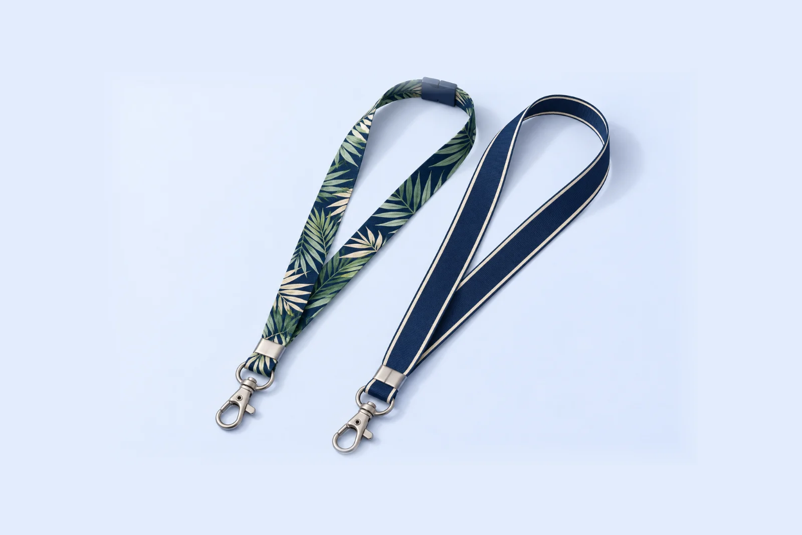 Two flat lanyards: a navy palm leaf print with a navy safety breakaway clip, and a solid navy woven ribbon with cream edge lines, each with a metal swivel hook
