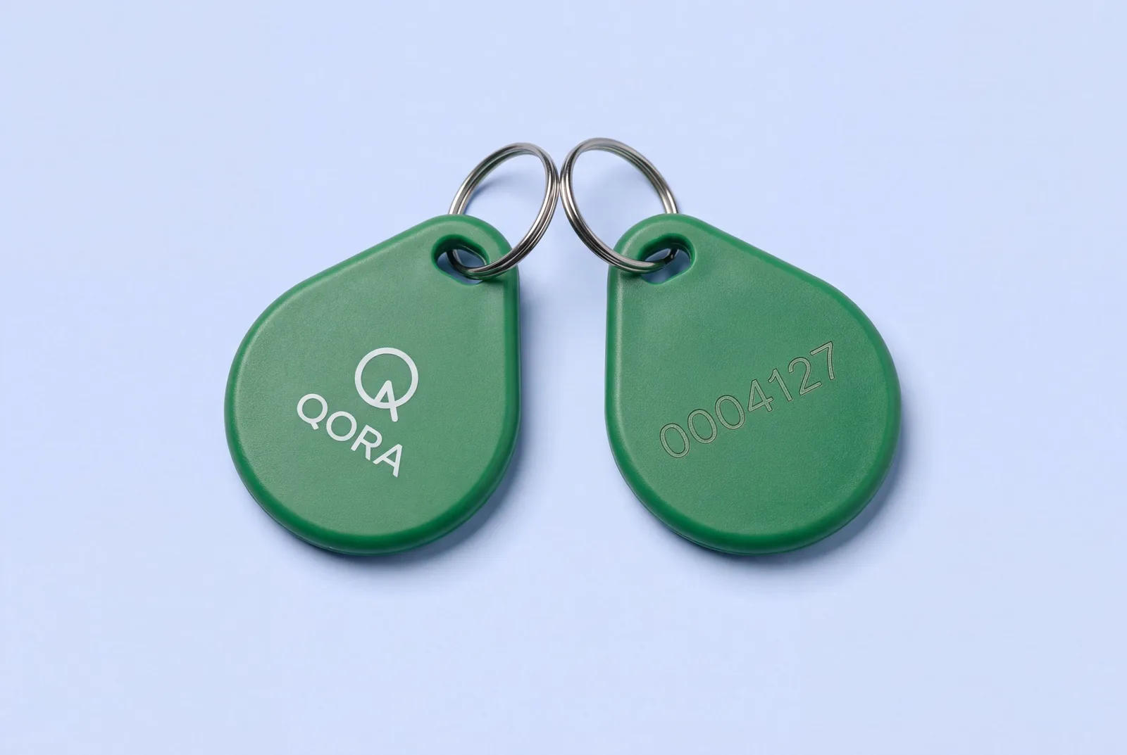 Two green ABS RFID key fobs on split rings, one printed QORA on the front, the other showing a laser engraved serial number on the back