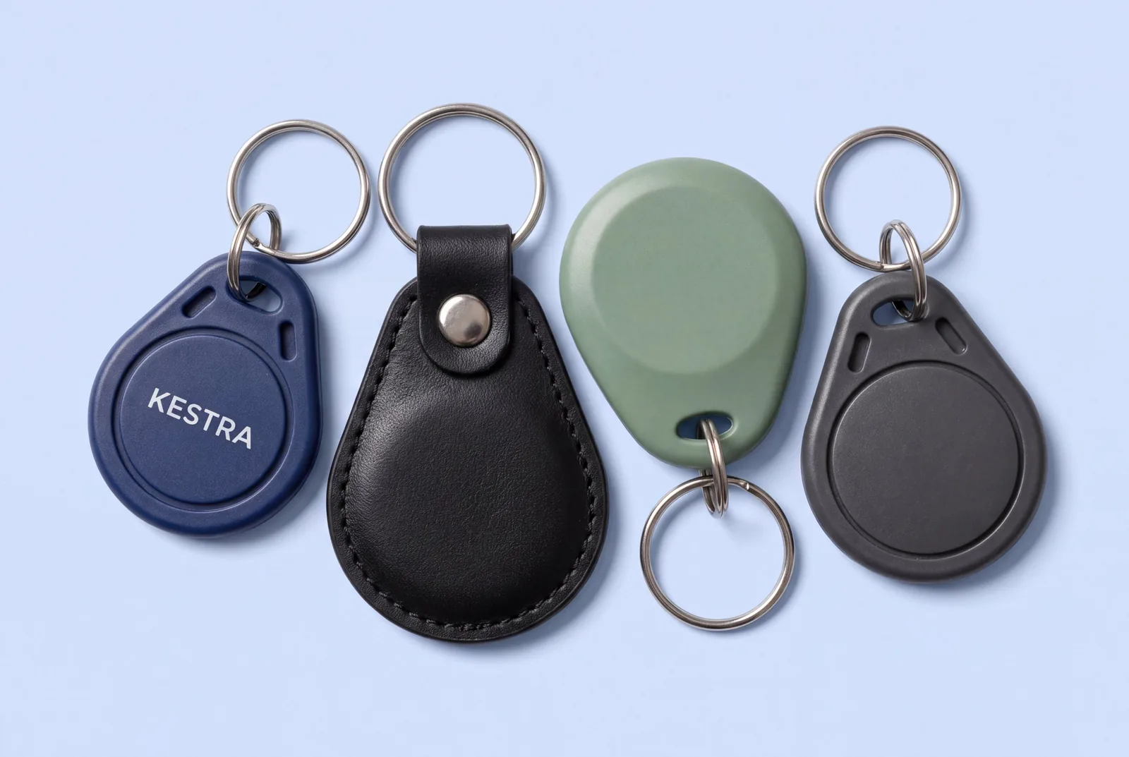 Four RFID key fobs on split rings: a navy ABS teardrop printed KESTRA, a black leather fob, a sage green fob and a charcoal teardrop