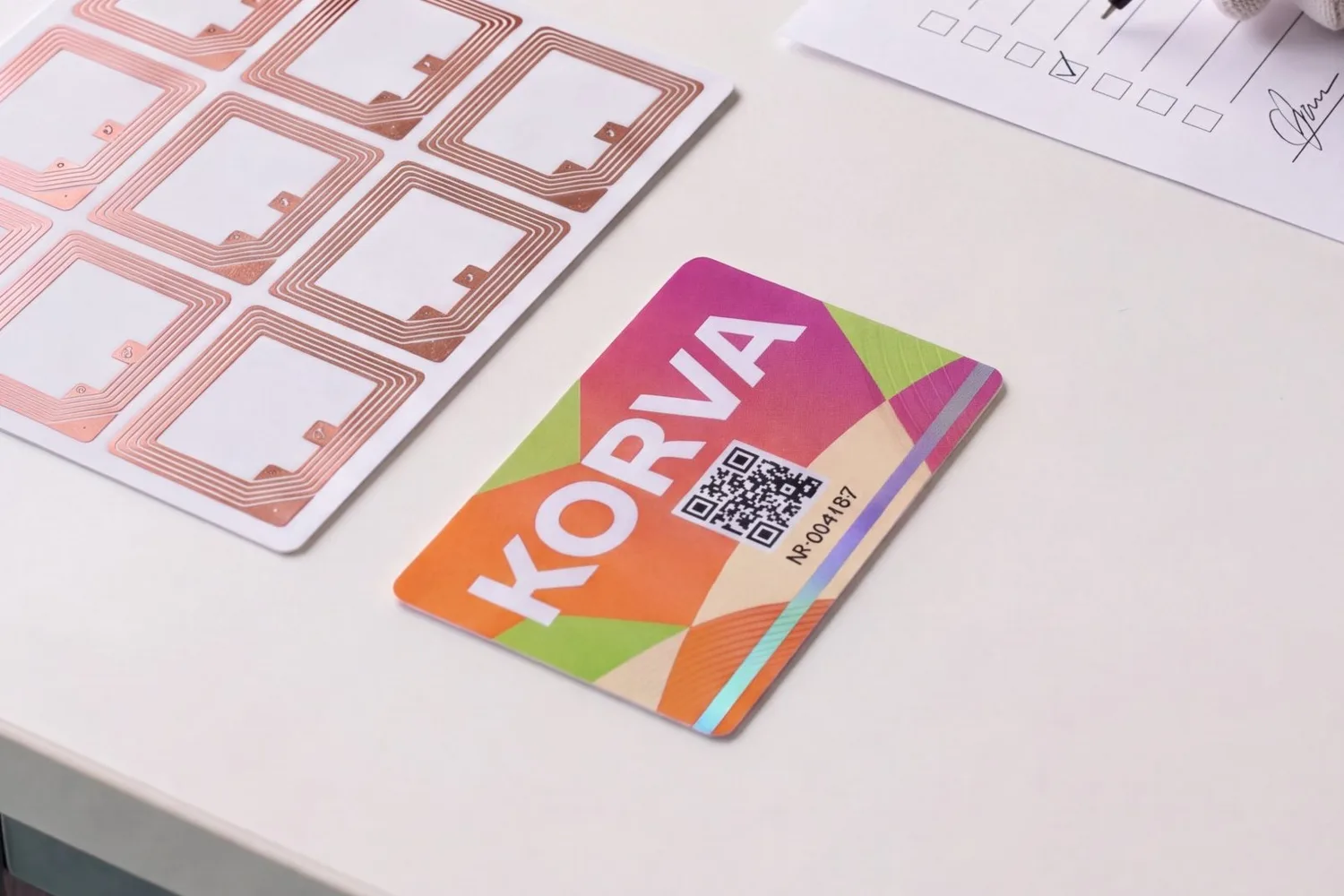 RFID inlay sheet with copper antennas beside a finished printed access card and a signed checklist