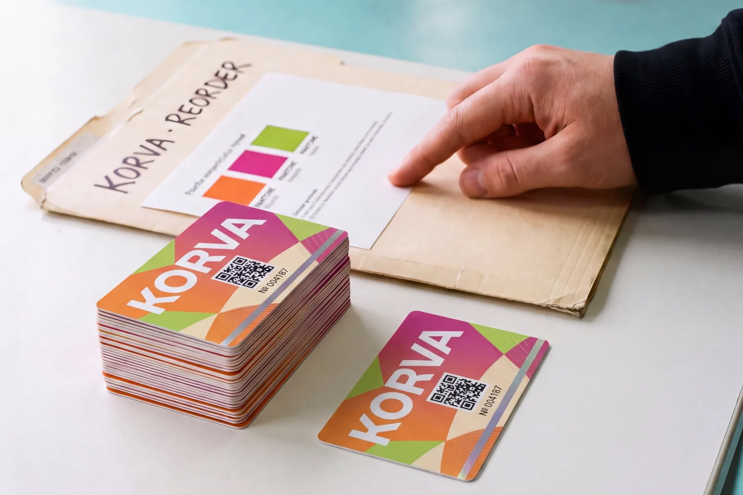 A stack of reordered PVC cards next to a card from the first run and the job folder with colour swatches