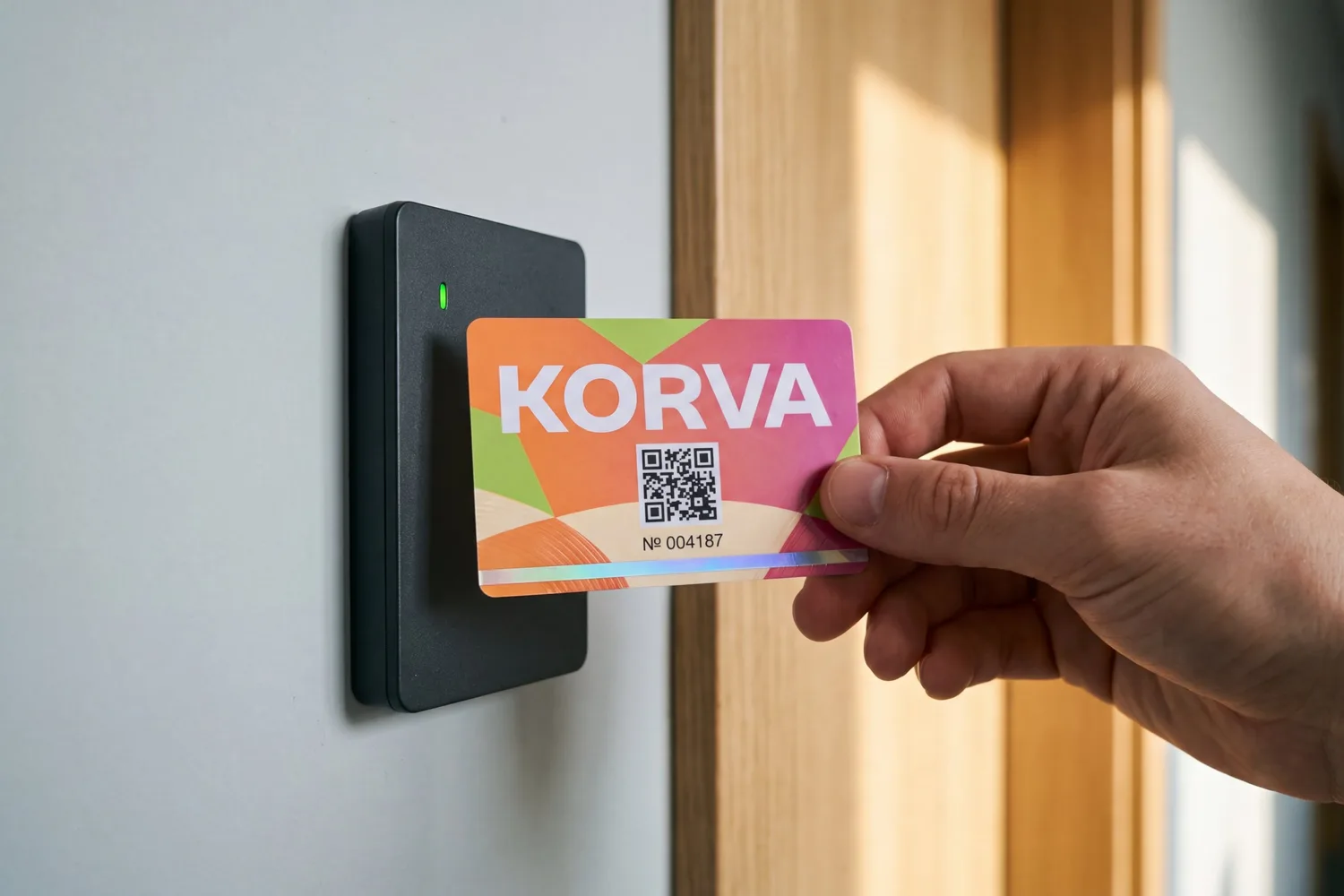A printed PVC access card held against a wall-mounted RFID reader with a green light