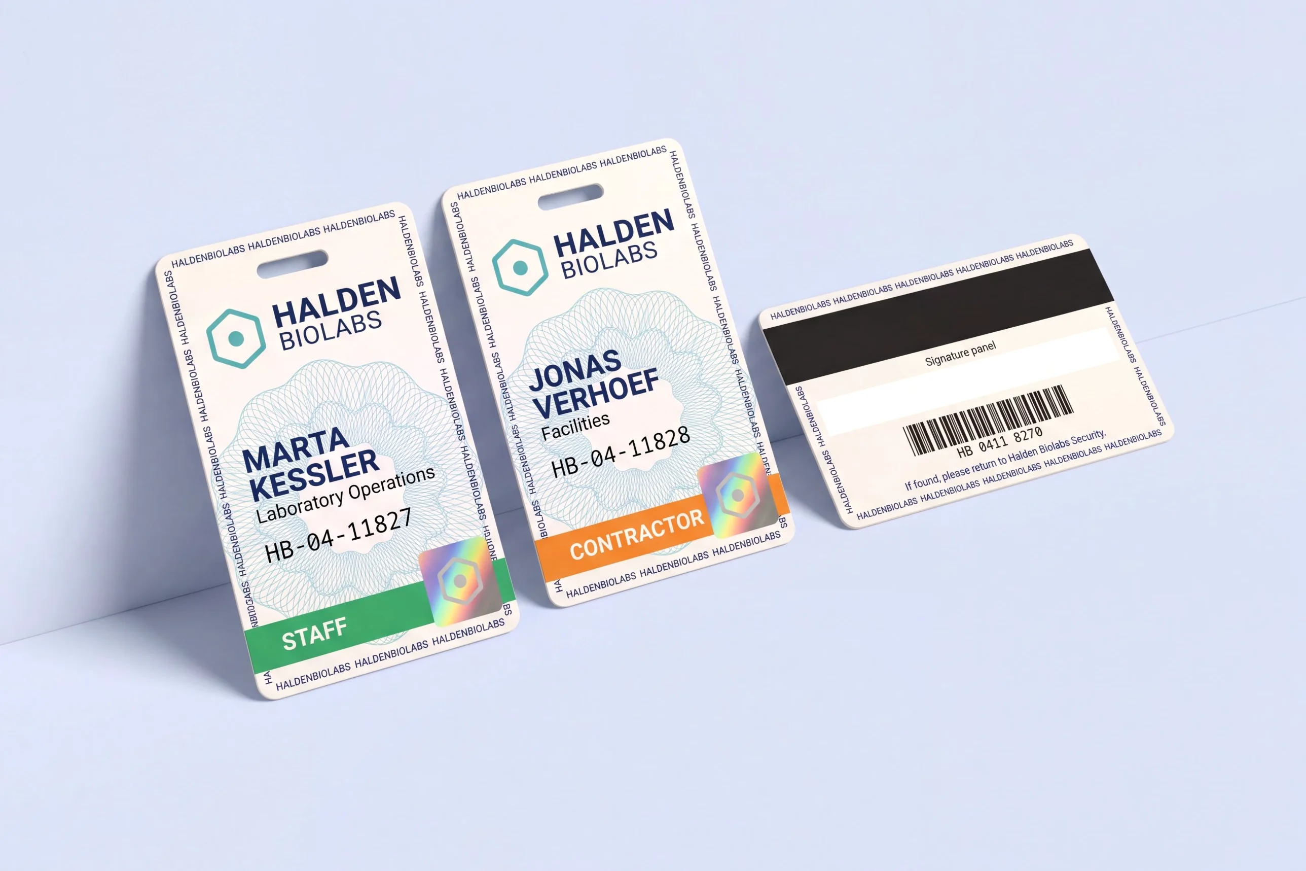 Two white security ID cards with a teal guilloche pattern, hologram patch and colour band, and the back of a third card with a magnetic stripe and barcode