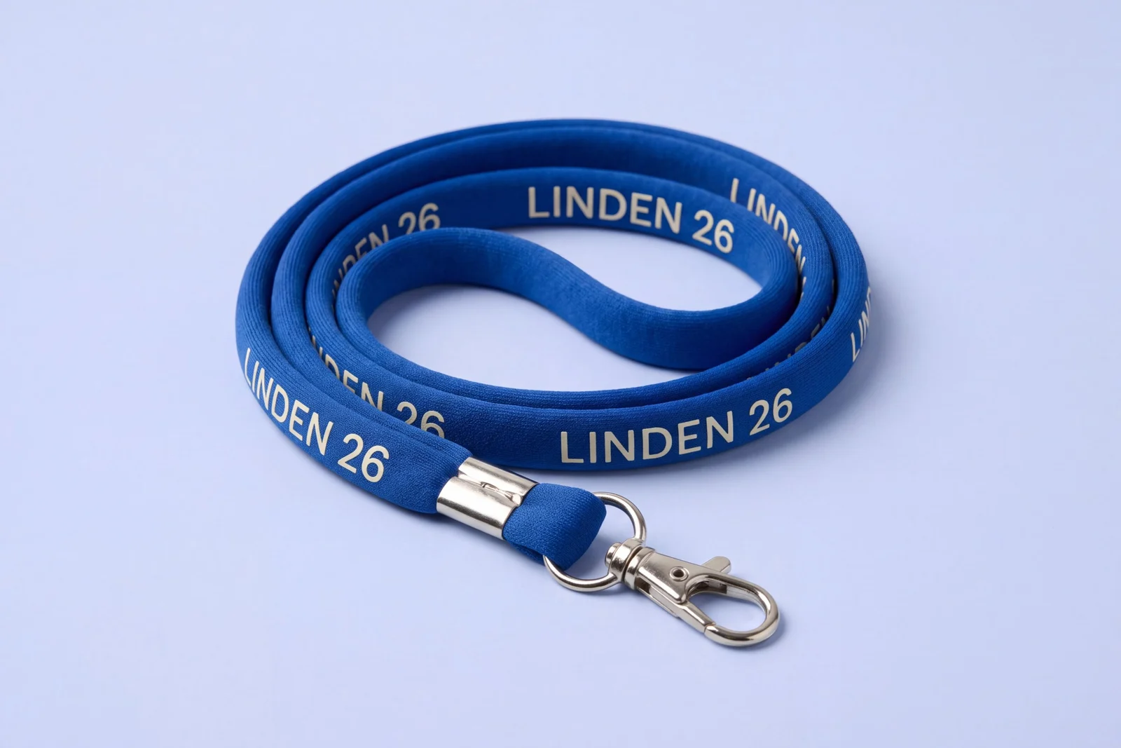 Cobalt blue tubular lanyard printed with a repeating event name in ivory, coiled flat, with a metal crimp and lobster clip