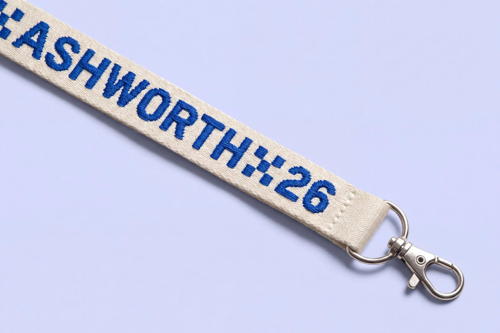 Close view of an ivory woven lanyard with the event name woven in cobalt blue thread, with a D-ring and lobster clip