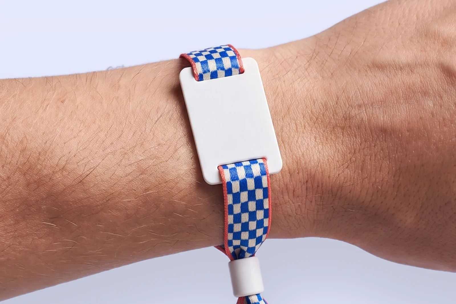 Fabric RFID wristband printed with a cobalt blue and ivory checkerboard with coral edges, a white PVC tag and a white closure, worn on a wrist