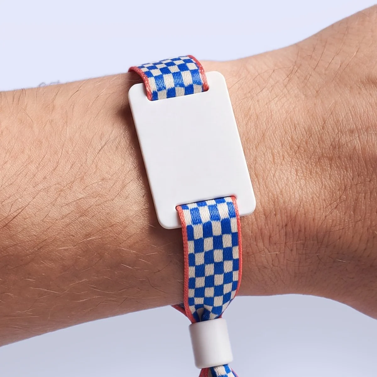 Fabric RFID wristband printed with a cobalt blue and ivory checkerboard with coral edges, a white PVC tag and a white closure, worn on a wrist