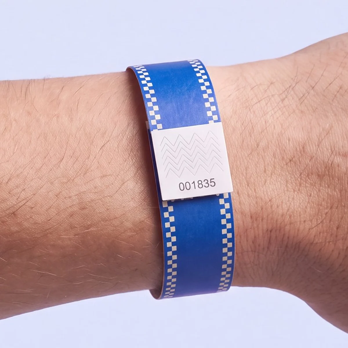 Tyvek RFID wristband printed in cobalt blue with ivory checkerboard edges, closed with a numbered white tab, worn on a wrist