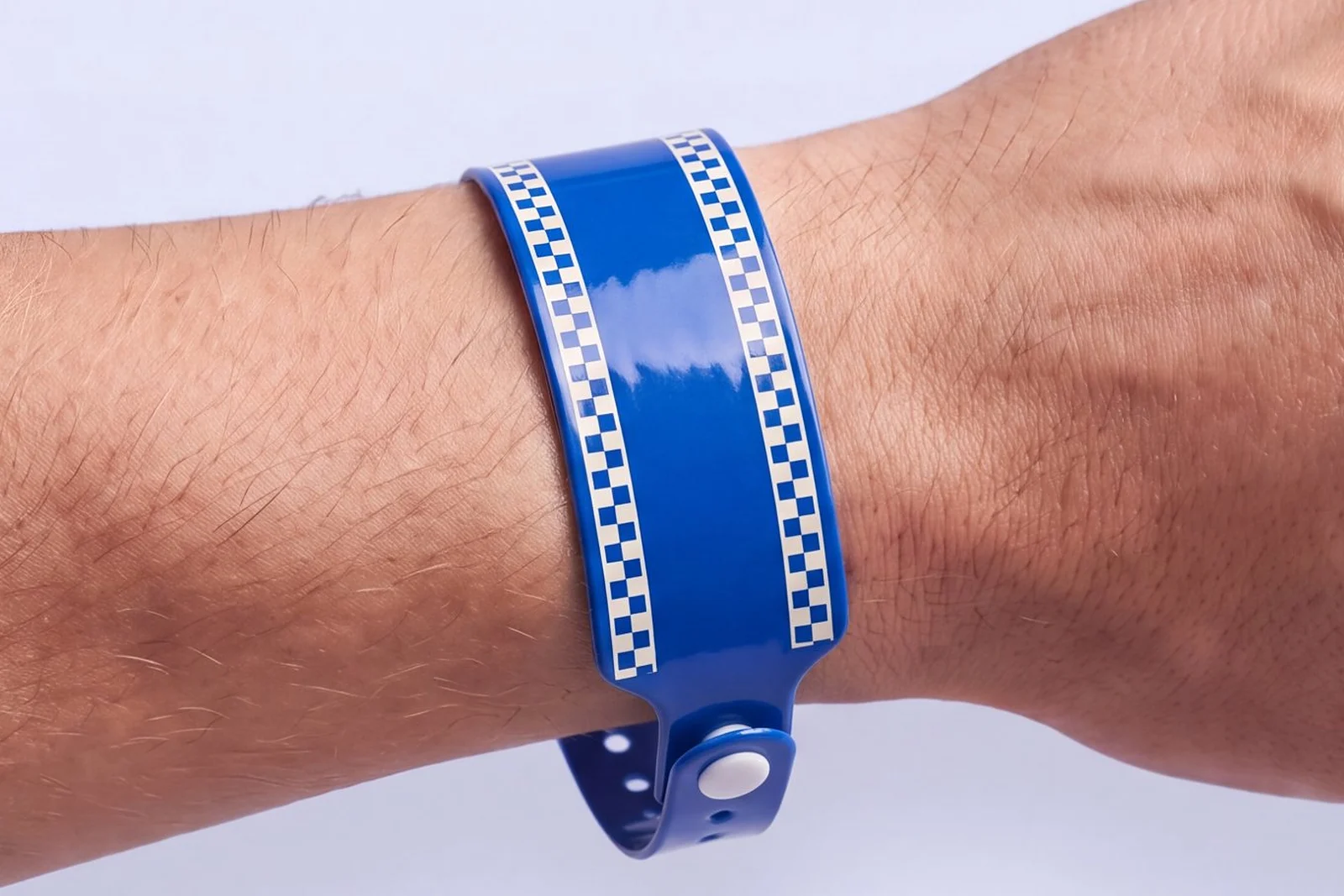 Cobalt blue vinyl RFID wristband with ivory checkerboard edges, closed with a white snap at the side of the wrist
