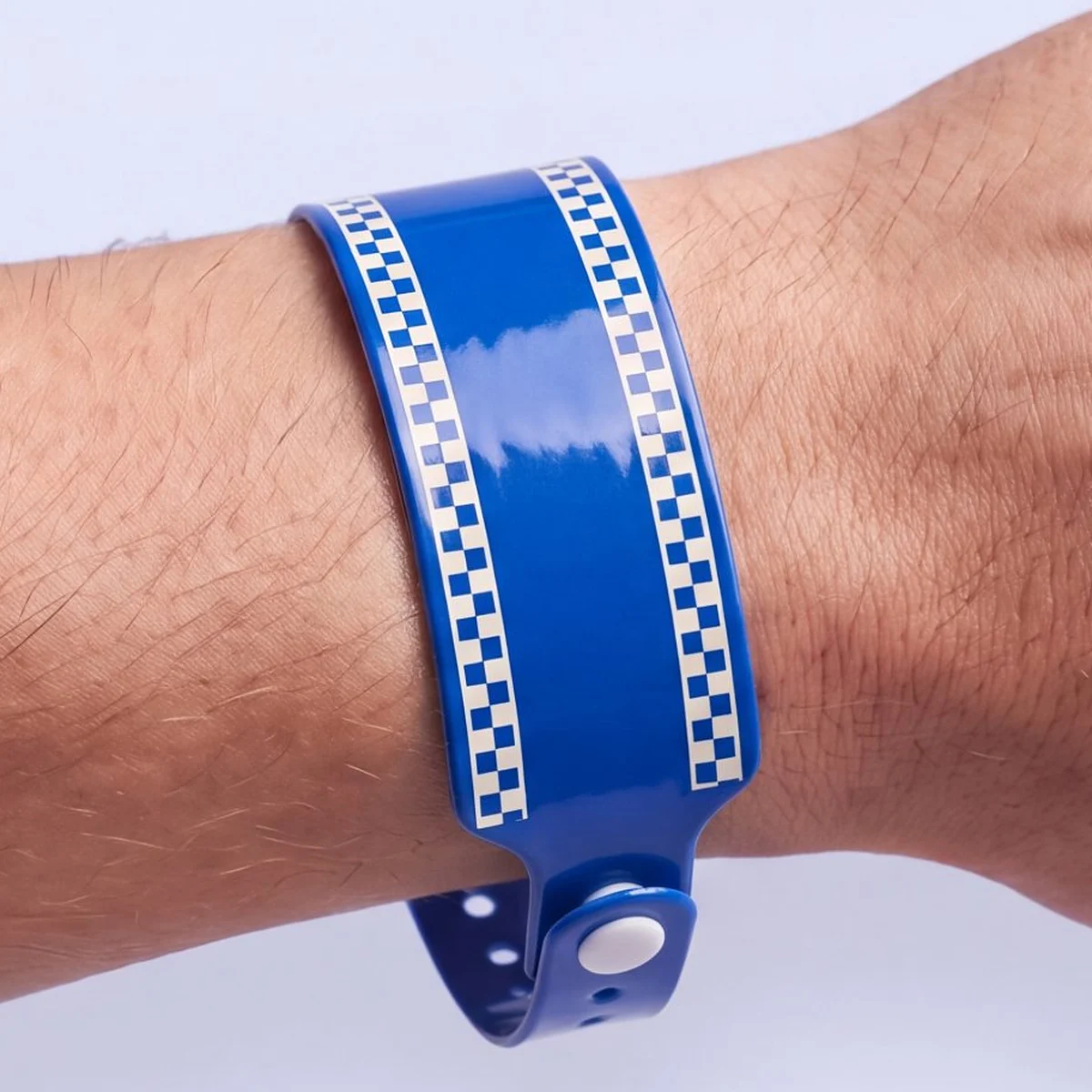 Cobalt blue vinyl RFID wristband with ivory checkerboard edges, closed with a white snap at the side of the wrist