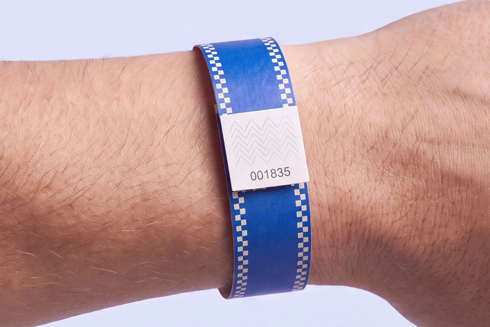 Tyvek RFID wristband printed in cobalt blue with ivory checkerboard edges, closed with a numbered white tab, worn on a wrist