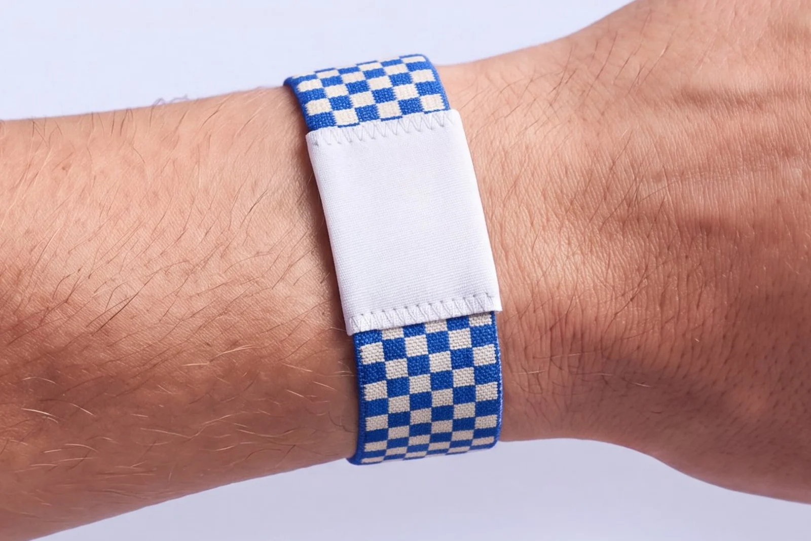 Stretch fabric RFID wristband woven in a cobalt blue and ivory checkerboard with a plain white fabric patch, worn on a wrist
