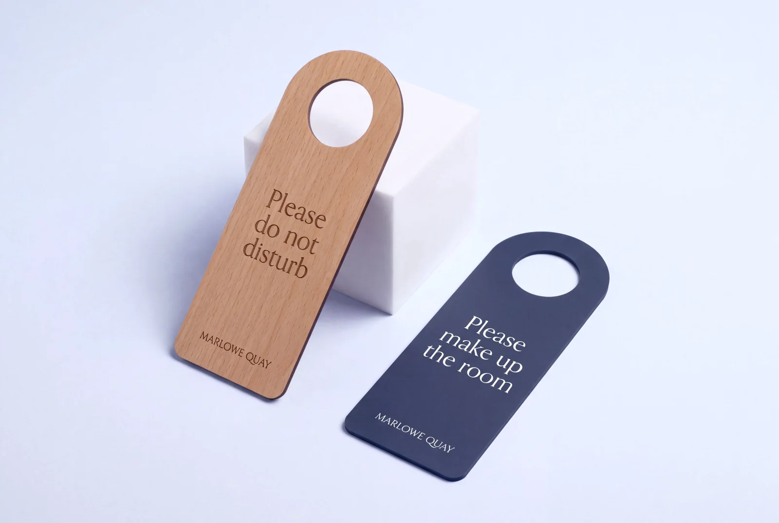 Two hotel door hangers, one in beech wood laser engraved and one in navy PVC printed in white